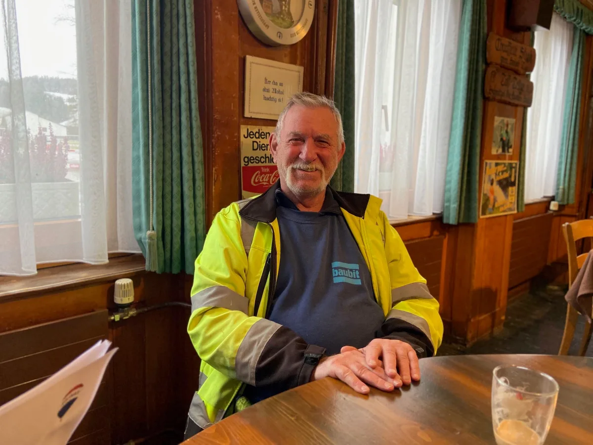 Alex Sommer sitzt am Stammtisch. Ein Mann mit neongelber Jacke.